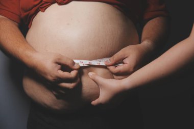 Asyalı şişman bir adam aynanın önünde vücuduna bakıyor. Aşırı göbek yağı, sağlıksız yaşam tarzı, diyet konsepti.