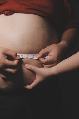 Asyalı şişman bir adam aynanın önünde vücuduna bakıyor. Aşırı göbek yağı, sağlıksız yaşam tarzı, diyet konsepti.