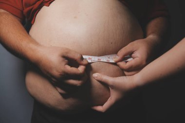 Asyalı şişman bir adam aynanın önünde vücuduna bakıyor. Aşırı göbek yağı, sağlıksız yaşam tarzı, diyet konsepti.