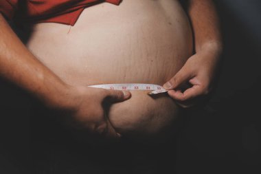 Asyalı şişman bir adam aynanın önünde vücuduna bakıyor. Aşırı göbek yağı, sağlıksız yaşam tarzı, diyet konsepti.