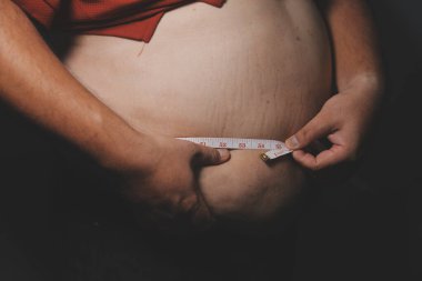 Asyalı şişman bir adam aynanın önünde vücuduna bakıyor. Aşırı göbek yağı, sağlıksız yaşam tarzı, diyet konsepti.