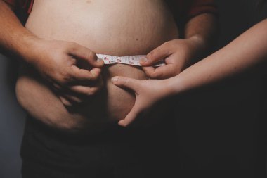 Asyalı şişman bir adam aynanın önünde vücuduna bakıyor. Aşırı göbek yağı, sağlıksız yaşam tarzı, diyet konsepti.