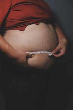 Asyalı şişman bir adam aynanın önünde vücuduna bakıyor. Aşırı göbek yağı, sağlıksız yaşam tarzı, diyet konsepti.