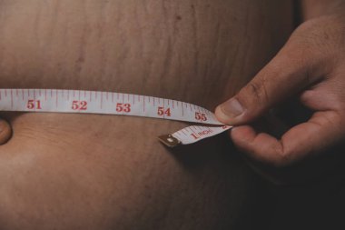 Asyalı şişman bir adam aynanın önünde vücuduna bakıyor. Aşırı göbek yağı, sağlıksız yaşam tarzı, diyet konsepti.