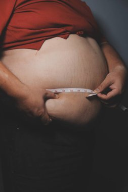 Asyalı şişman bir adam aynanın önünde vücuduna bakıyor. Aşırı göbek yağı, sağlıksız yaşam tarzı, diyet konsepti.