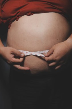 Asyalı şişman bir adam aynanın önünde vücuduna bakıyor. Aşırı göbek yağı, sağlıksız yaşam tarzı, diyet konsepti.