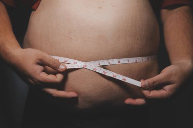 Asyalı şişman bir adam aynanın önünde vücuduna bakıyor. Aşırı göbek yağı, sağlıksız yaşam tarzı, diyet konsepti.