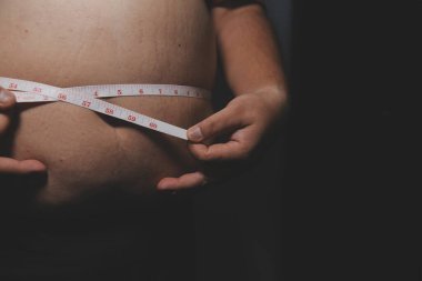 Asyalı şişman bir adam aynanın önünde vücuduna bakıyor. Aşırı göbek yağı, sağlıksız yaşam tarzı, diyet konsepti.