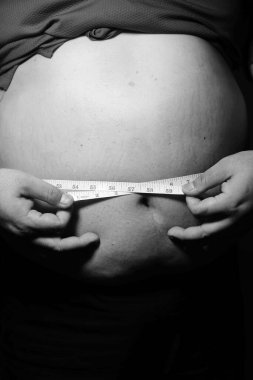 Asyalı şişman bir adam aynanın önünde vücuduna bakıyor. Aşırı göbek yağı, sağlıksız yaşam tarzı, diyet konsepti.