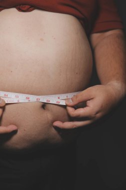 Asyalı şişman bir adam aynanın önünde vücuduna bakıyor. Aşırı göbek yağı, sağlıksız yaşam tarzı, diyet konsepti.