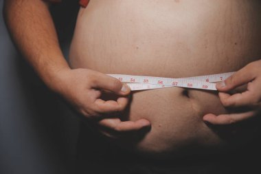 Asyalı şişman bir adam aynanın önünde vücuduna bakıyor. Aşırı göbek yağı, sağlıksız yaşam tarzı, diyet konsepti.