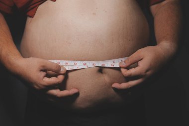 Asyalı şişman bir adam aynanın önünde vücuduna bakıyor. Aşırı göbek yağı, sağlıksız yaşam tarzı, diyet konsepti.