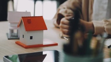 Evin modelini tutan ve evin planını masaya koyan adam.