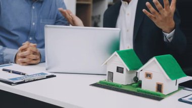 Takım elbiseli iş adamı ev modelini tutuyor ve başparmağını gösteriyor.