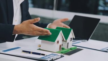 Emlakçı ya da emlakçı ev modelini elinde tutuyor.