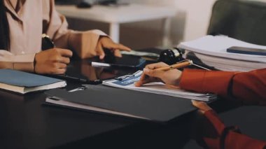 Siyah takım elbiseli ve beyaz gömlekli genç bir kadın masada oturuyor ve ofisteki bir dizüstü bilgisayarın üzerinde çalışıyor.