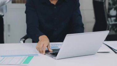 Elinde bir belge tutan ve dizüstü bilgisayarı işaret eden bir iş adamı.