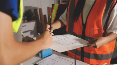 İnşaat kaskındaki kadın mühendis elinde kağıt planlar ve şantiyede çalışıyor..