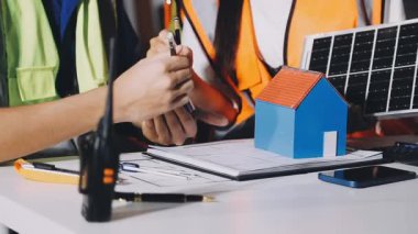 İnsan mühendisi ya da işçi ev modelini ve elektrik prizi ve evdeki güneş enerjisi santrali için güneş enerjisi sistemine sahip güneş panelini masasında tutuyor.