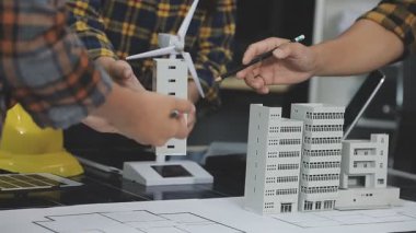 Adam mimar ev projesi üzerinde çalışıyor. Masada model var. Model konsepti inşa ediyor.