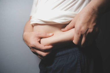 Asyalı şişman bir adam aynanın önünde vücuduna bakıyor. Aşırı göbek yağı, sağlıksız yaşam tarzı, diyet konsepti.