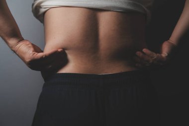 Asyalı şişman bir adam aynanın önünde vücuduna bakıyor. Aşırı göbek yağı, sağlıksız yaşam tarzı, diyet konsepti.