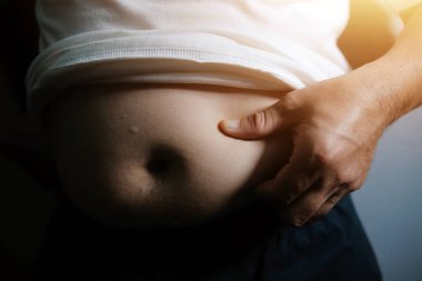 Asyalı şişman bir adam aynanın önünde vücuduna bakıyor. Aşırı göbek yağı, sağlıksız yaşam tarzı, diyet konsepti.