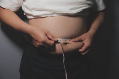 Asyalı şişman bir adam aynanın önünde vücuduna bakıyor. Aşırı göbek yağı, sağlıksız yaşam tarzı, diyet konsepti.