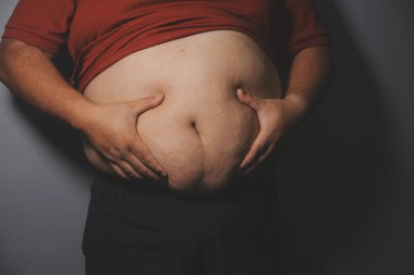 Asyalı şişman bir adam aynanın önünde vücuduna bakıyor. Aşırı göbek yağı, sağlıksız yaşam tarzı, diyet konsepti.