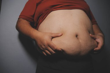 Asyalı şişman bir adam aynanın önünde vücuduna bakıyor. Aşırı göbek yağı, sağlıksız yaşam tarzı, diyet konsepti.