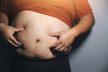 Asyalı şişman bir adam aynanın önünde vücuduna bakıyor. Aşırı göbek yağı, sağlıksız yaşam tarzı, diyet konsepti.