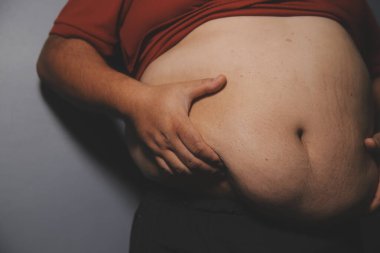 Asyalı şişman bir adam aynanın önünde vücuduna bakıyor. Aşırı göbek yağı, sağlıksız yaşam tarzı, diyet konsepti.