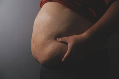 Asyalı şişman bir adam aynanın önünde vücuduna bakıyor. Aşırı göbek yağı, sağlıksız yaşam tarzı, diyet konsepti.