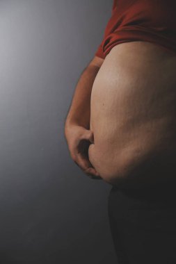 Asyalı şişman bir adam aynanın önünde vücuduna bakıyor. Aşırı göbek yağı, sağlıksız yaşam tarzı, diyet konsepti.