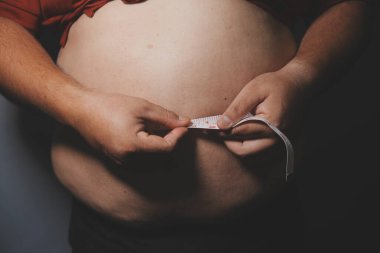 Asyalı şişman bir adam aynanın önünde vücuduna bakıyor. Aşırı göbek yağı, sağlıksız yaşam tarzı, diyet konsepti.