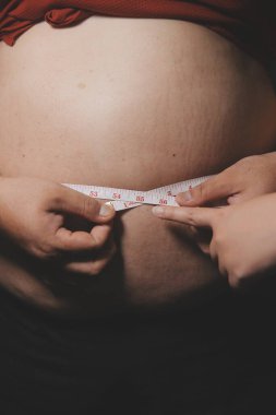 Asyalı şişman bir adam aynanın önünde vücuduna bakıyor. Aşırı göbek yağı, sağlıksız yaşam tarzı, diyet konsepti.