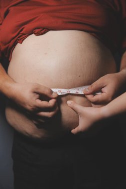 Asyalı şişman bir adam aynanın önünde vücuduna bakıyor. Aşırı göbek yağı, sağlıksız yaşam tarzı, diyet konsepti.