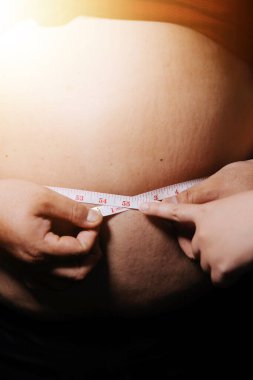 Asyalı şişman bir adam aynanın önünde vücuduna bakıyor. Aşırı göbek yağı, sağlıksız yaşam tarzı, diyet konsepti.