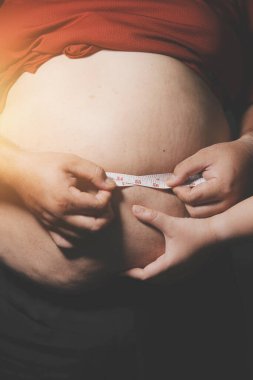 Asyalı şişman bir adam aynanın önünde vücuduna bakıyor. Aşırı göbek yağı, sağlıksız yaşam tarzı, diyet konsepti.