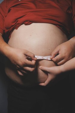 Asyalı şişman bir adam aynanın önünde vücuduna bakıyor. Aşırı göbek yağı, sağlıksız yaşam tarzı, diyet konsepti.