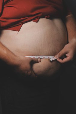 Asyalı şişman bir adam aynanın önünde vücuduna bakıyor. Aşırı göbek yağı, sağlıksız yaşam tarzı, diyet konsepti.