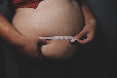 Asyalı şişman bir adam aynanın önünde vücuduna bakıyor. Aşırı göbek yağı, sağlıksız yaşam tarzı, diyet konsepti.