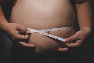 Asyalı şişman bir adam aynanın önünde vücuduna bakıyor. Aşırı göbek yağı, sağlıksız yaşam tarzı, diyet konsepti.