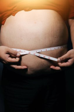 Asyalı şişman bir adam aynanın önünde vücuduna bakıyor. Aşırı göbek yağı, sağlıksız yaşam tarzı, diyet konsepti.