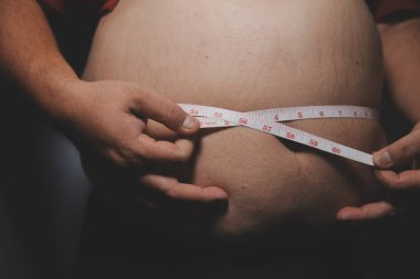 Asyalı şişman bir adam aynanın önünde vücuduna bakıyor. Aşırı göbek yağı, sağlıksız yaşam tarzı, diyet konsepti.