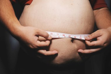 Asyalı şişman bir adam aynanın önünde vücuduna bakıyor. Aşırı göbek yağı, sağlıksız yaşam tarzı, diyet konsepti.