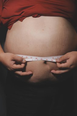 Asyalı şişman bir adam aynanın önünde vücuduna bakıyor. Aşırı göbek yağı, sağlıksız yaşam tarzı, diyet konsepti.