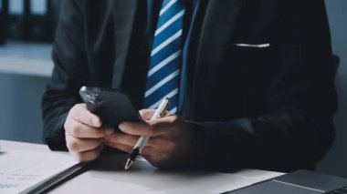 Genç iş adamı ofiste dizüstü bilgisayarla çalışıyor. Adam akıllı telefon kullanıyor.