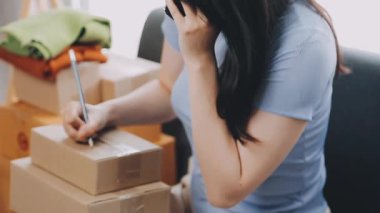 Kadın bir paket tutuyor ve müşterilerine bir paket göndermek için akıllı telefon kullanıyor..