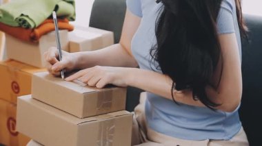 Genç, güzel Asyalı kadın oturma odasında paket paketliyor.